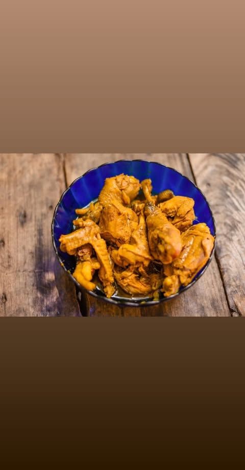 Uma tigela com pedaços de frango dourados repousa sobre uma mesa rústica de madeira.