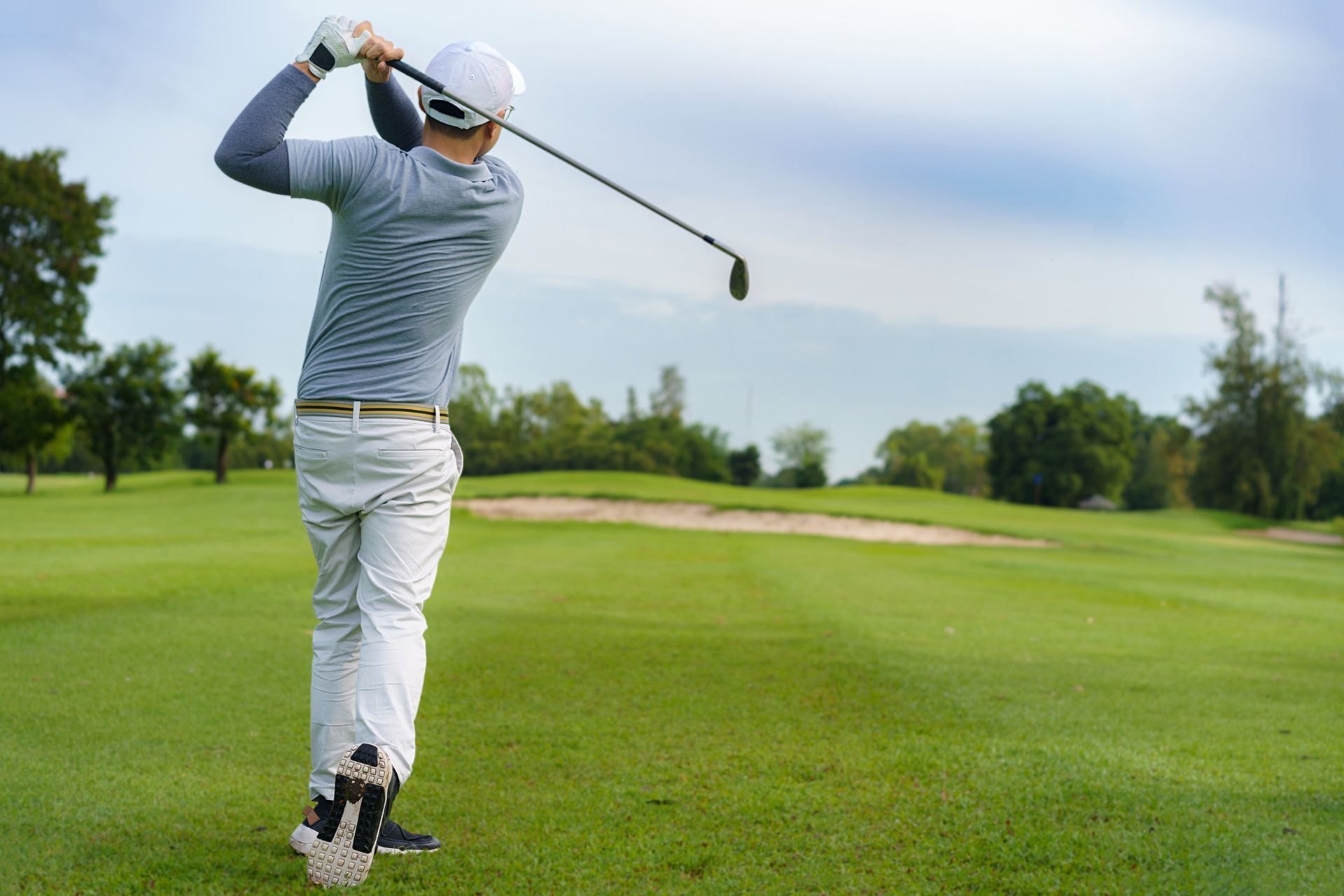 A man is swinging a golf club on a golf course. - Your South Florida Real Estate Expert