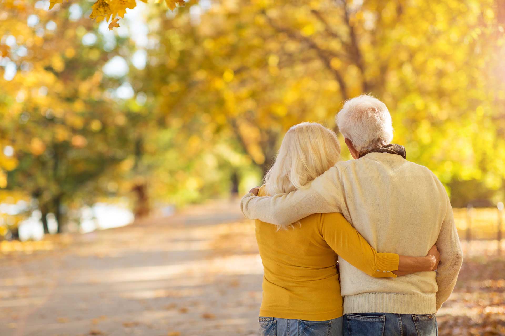 Older couple walking arm in arm through autumn trees in Midvale, Utah, representing comfort and care
