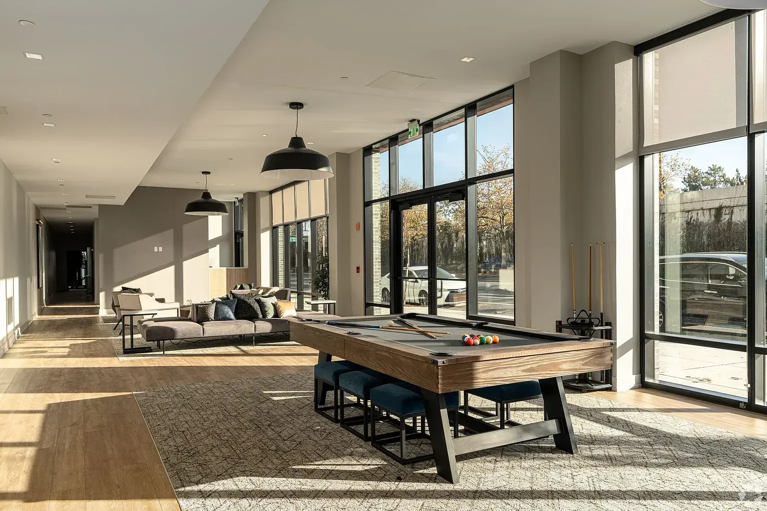 Photo of a community lounge with a pool table in the foreground and pelnty of natural lighting