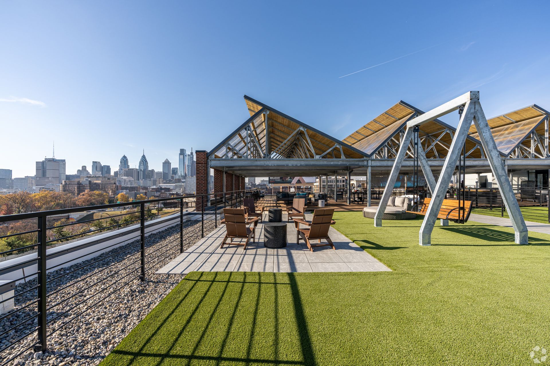 Photo of a rooftop lounge showing a firepit area, a large swinging bench and plenty of seating in the background