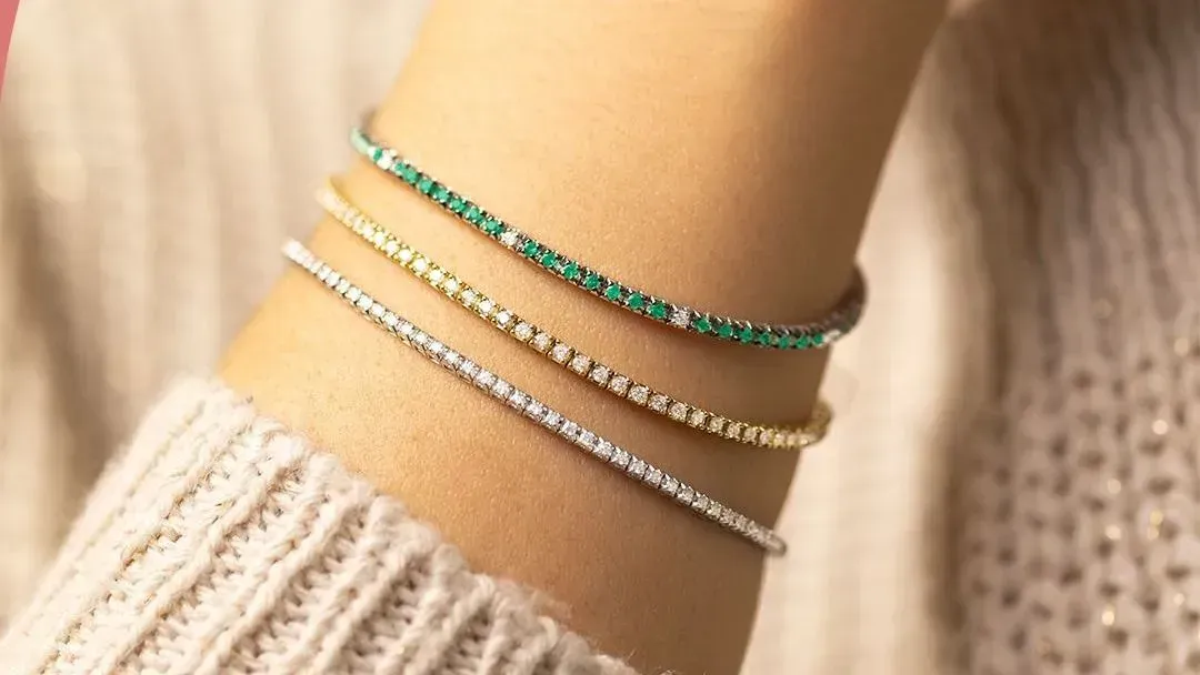 Primo piano di tre sottili bracciali su un polso: smeraldo, oro e diamanti.