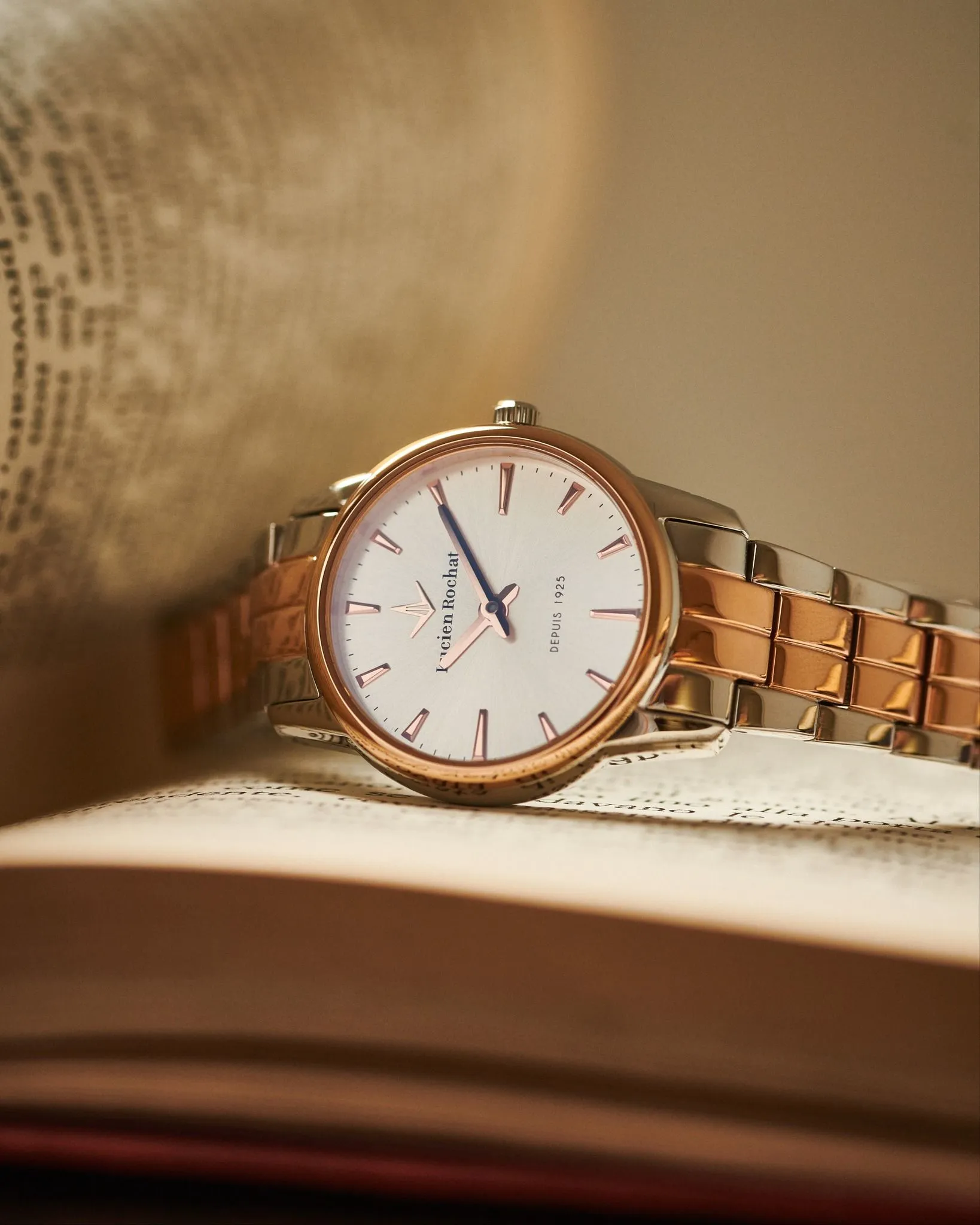 Orologio da polso con cinturino in oro e argento appoggiato su un libro aperto, accanto a un mappamondo sfocato.