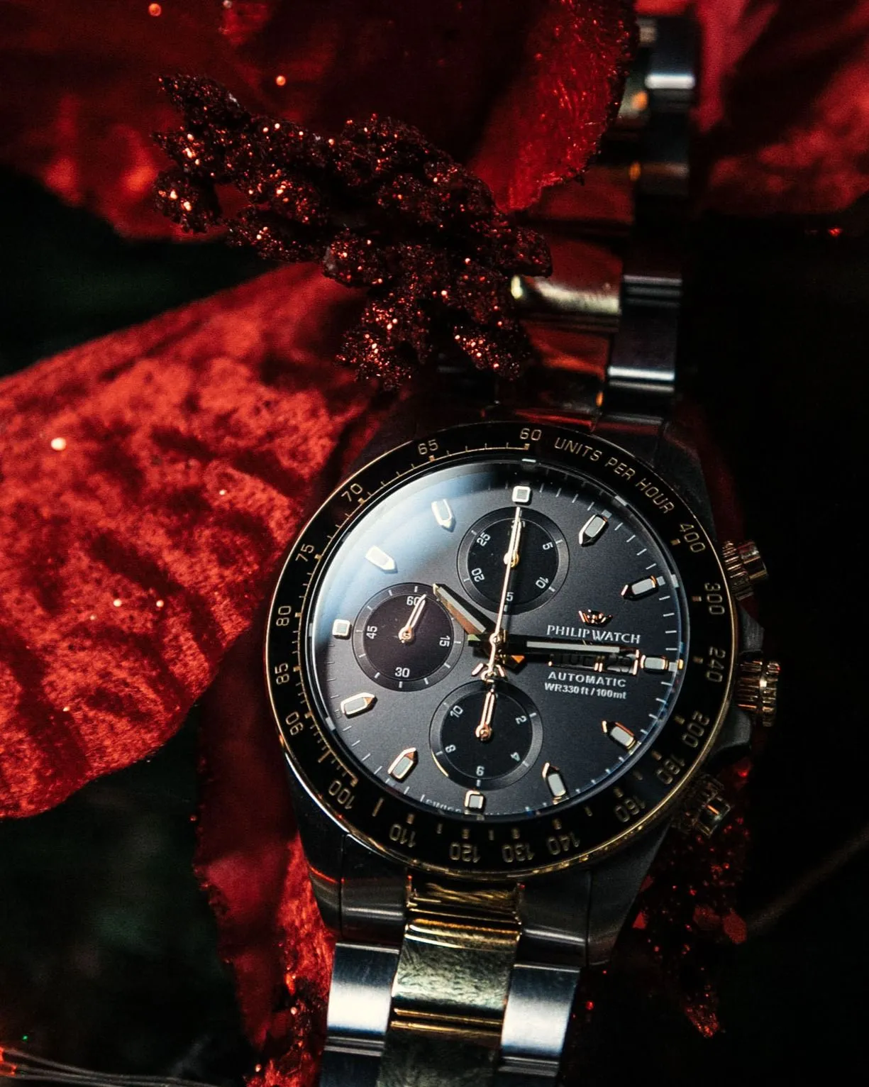 Orologio da polso bicolore con quadrante nero e dettagli dorati, incastonato su un fiore rosso scintillante.