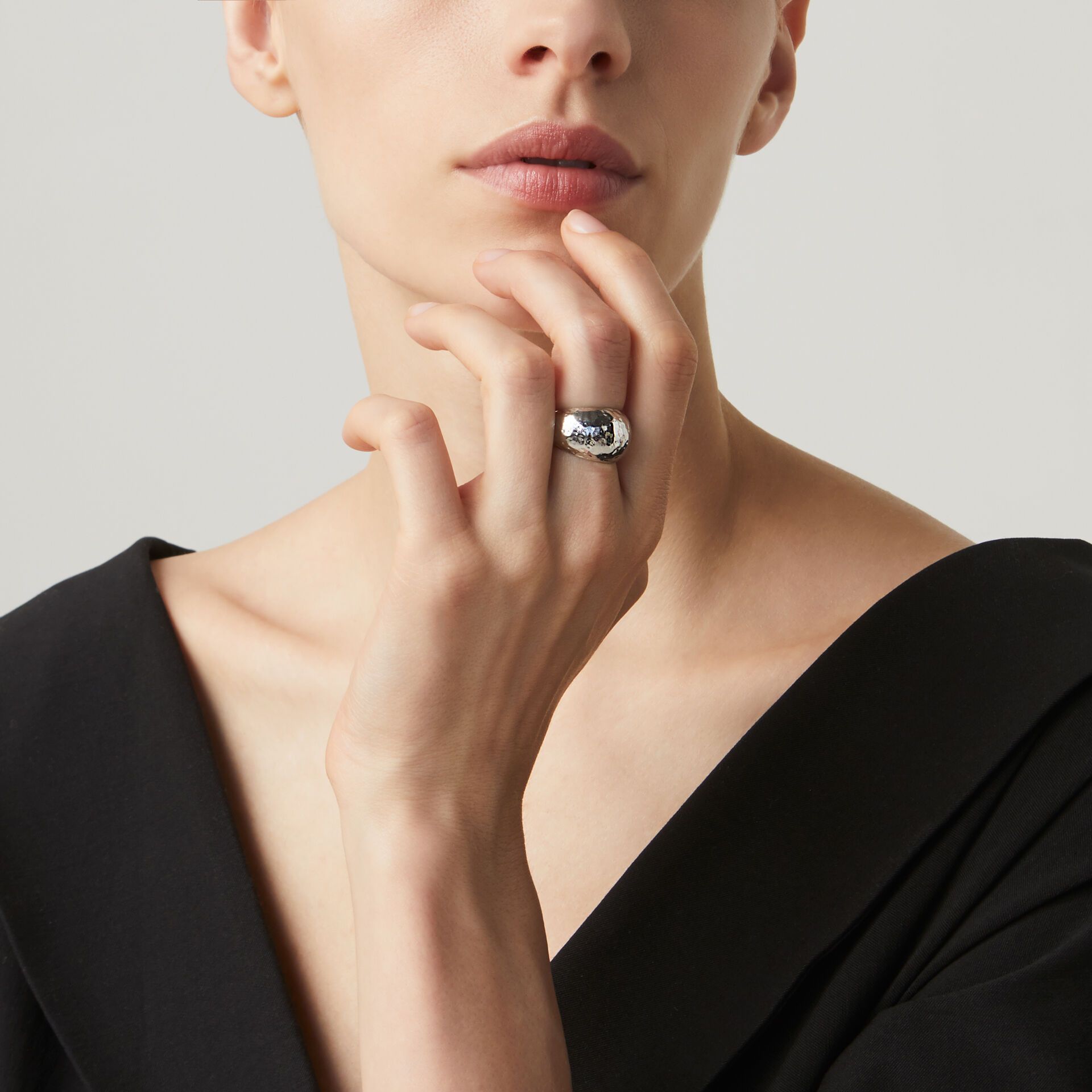 Donna con anello d'argento, mento appoggiato sulla mano. Top nero, sfondo neutro.