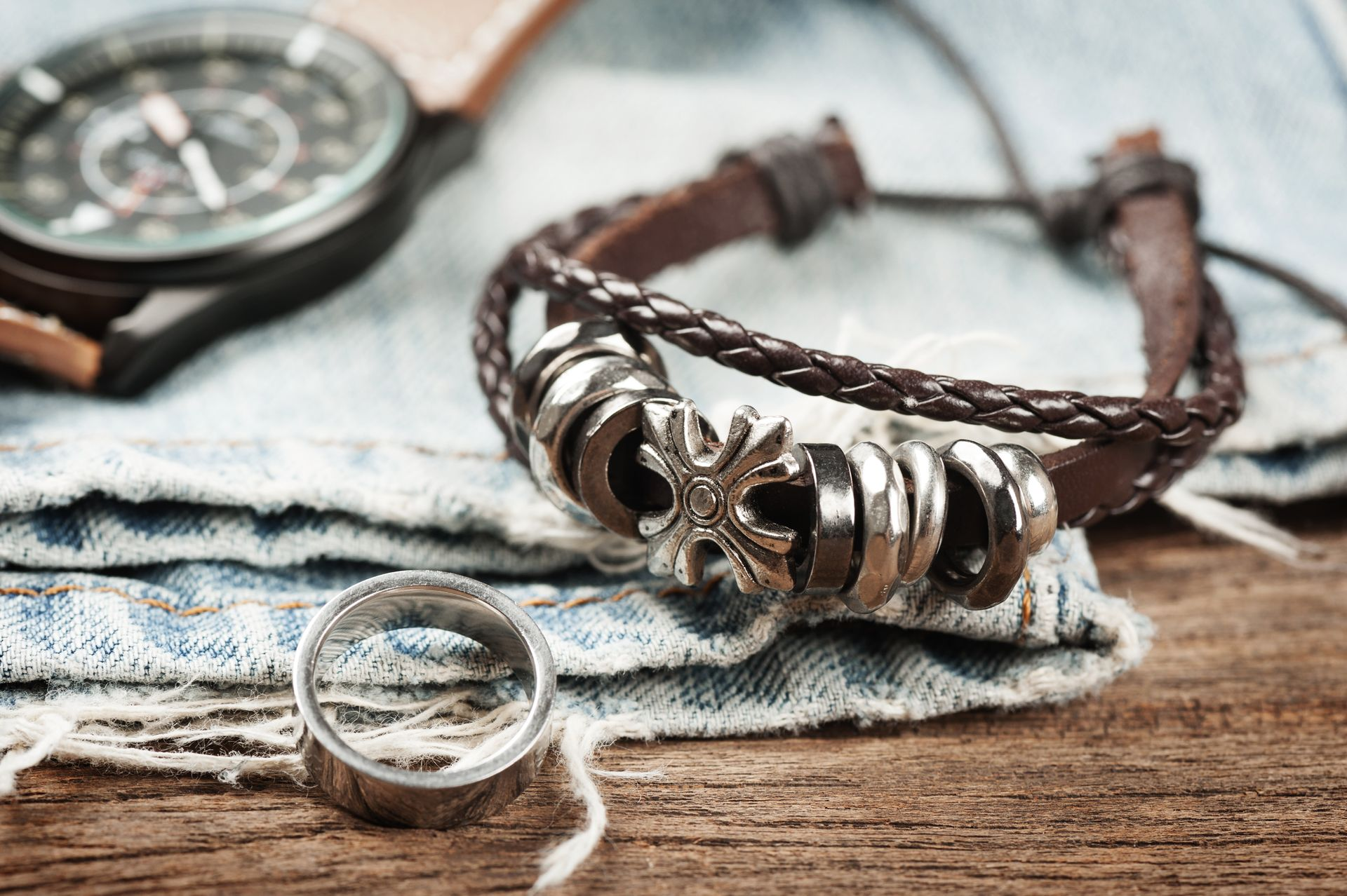 Orologio, bracciale in pelle con dettagli in metallo e anello in argento su tessuto denim.