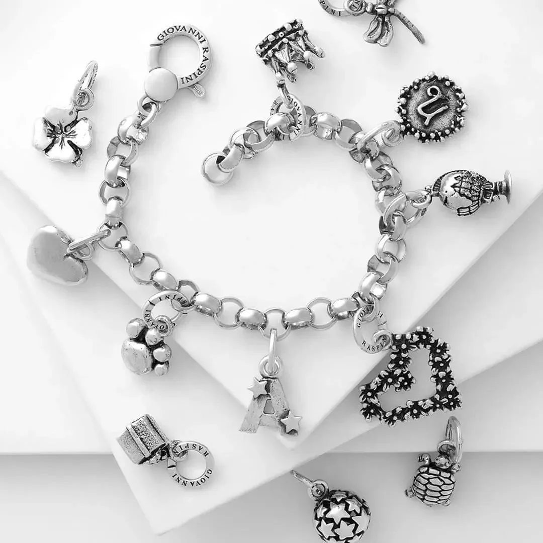 Braccialetto in argento con vari ciondoli decorativi disposti su una superficie bianca.