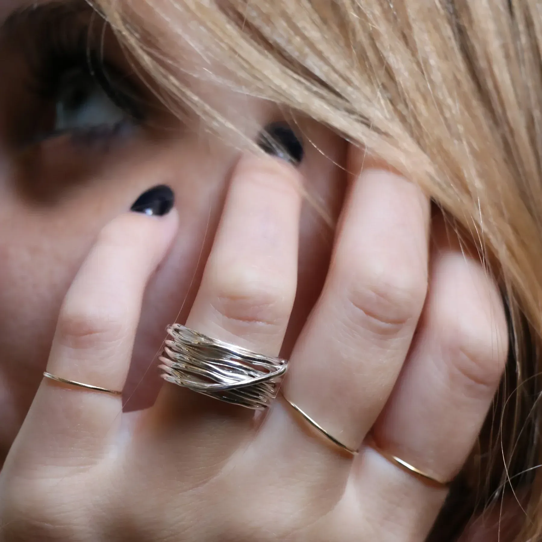 Mano di donna con smalto nero e diversi anelli sulle dita, vicino al viso.
