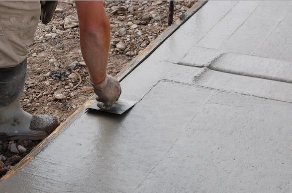 A person is spreading concrete on a sidewalk with a trowel.