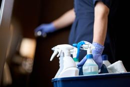 A woman is carrying a bucket of cleaning supplies.