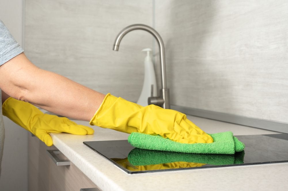 A person wearing yellow gloves is cleaning a kitchen counter with a green cloth.