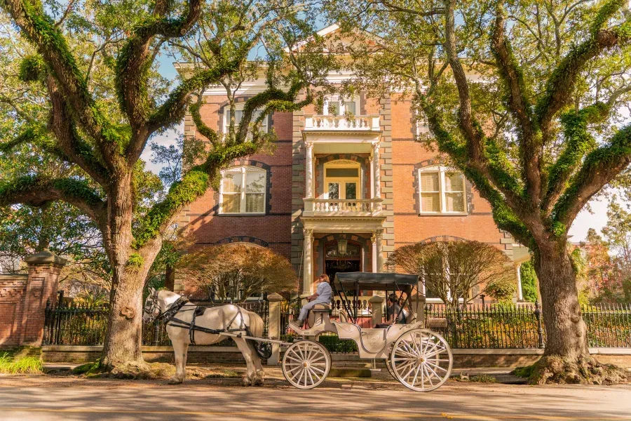 A horse drawn carriage is parked in front of a large brick building.