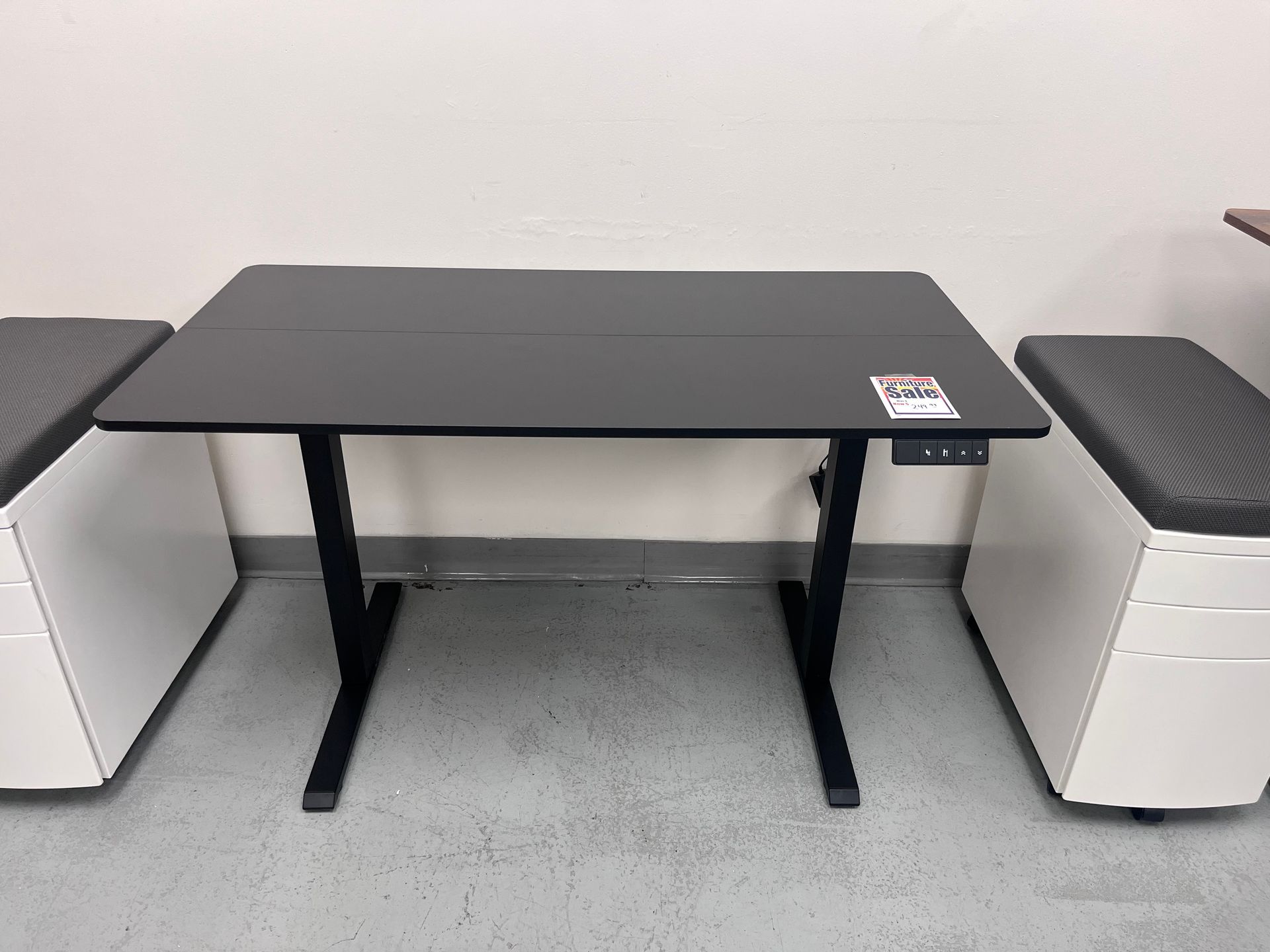 Black adjustable height desk, with white storage units, set in a room with a concrete floor.
