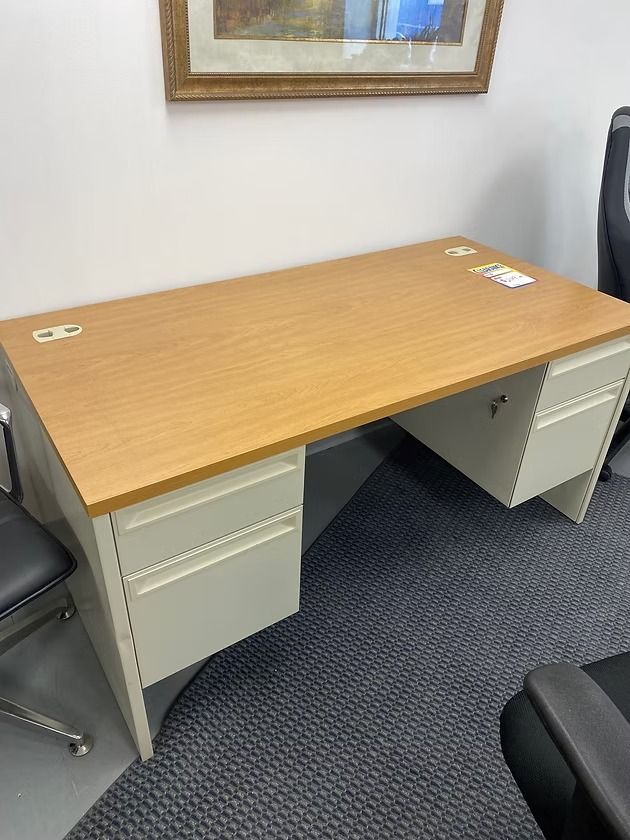 Tan office desk with light gray metal drawers, on a dark carpet. A framed picture hangs above.