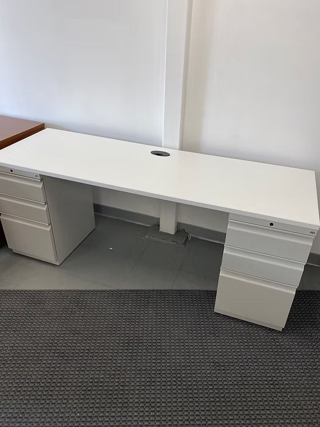 White office desk with drawers, cable hole, and gray carpet.