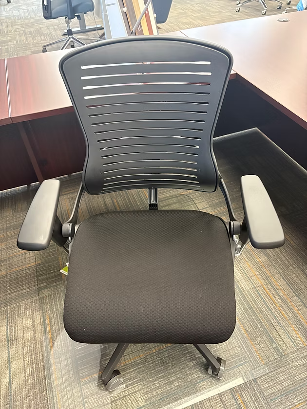 Black office chair with mesh back and padded seat, in front of a desk.