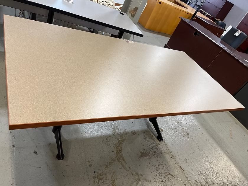 Tan rectangular office table with black legs, in a room with other furniture.