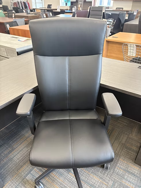 Black office chair with high back, gray arms, and rolling base, in an office.