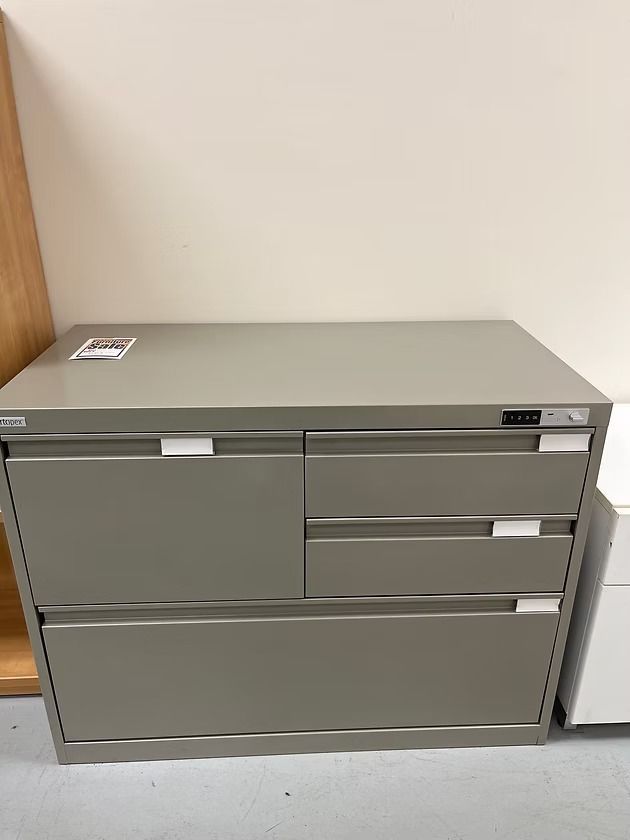 Gray metal filing cabinet with four drawers, in an office setting.
