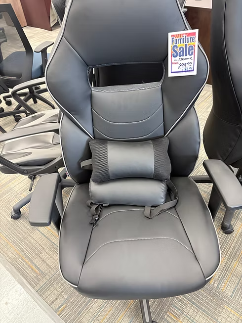 Black and gray ergonomic office chair with a lumbar pillow on a showroom floor.