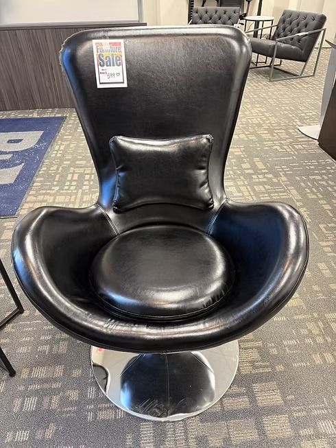 Black leather swivel chair with a lumbar pillow, on a silver base, in a showroom.