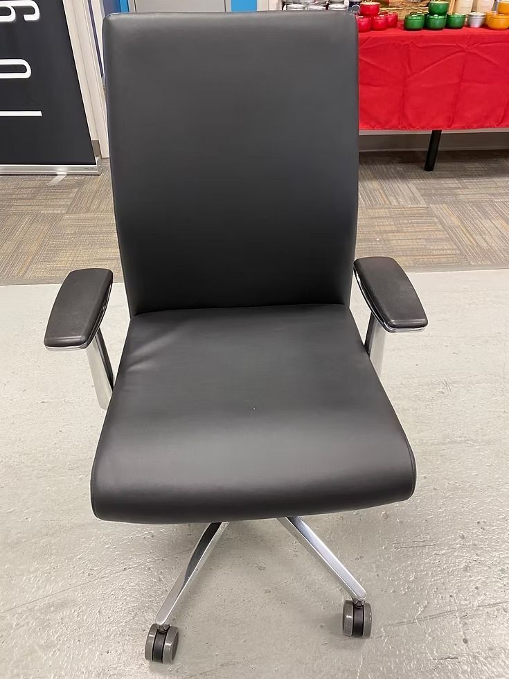 Black leather office chair with silver base and armrests, sitting on wheels.