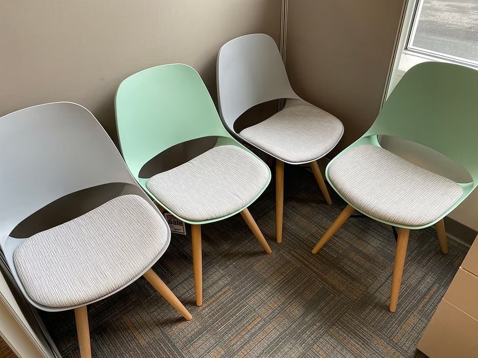 Four modern chairs in shades of gray and mint green, with light wood legs, arranged in a room.