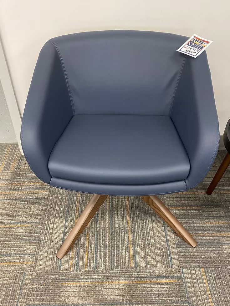 Blue upholstered chair with wooden base on patterned carpet.