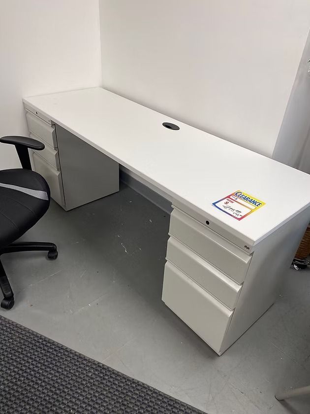 White office desk with drawers, black office chair, and gray flooring.