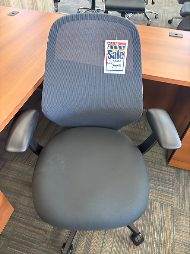 Gray office chair with mesh back and adjustable arms, placed by a desk.