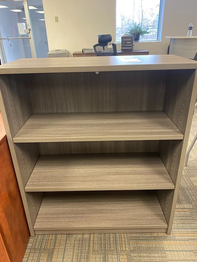Three-shelf, gray wooden bookcase in an office setting.