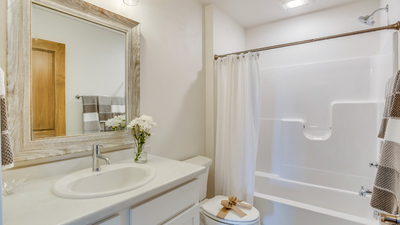 Bathroom with white vanity, sink, toilet, and shower/tub. A bouquet sits on the counter.