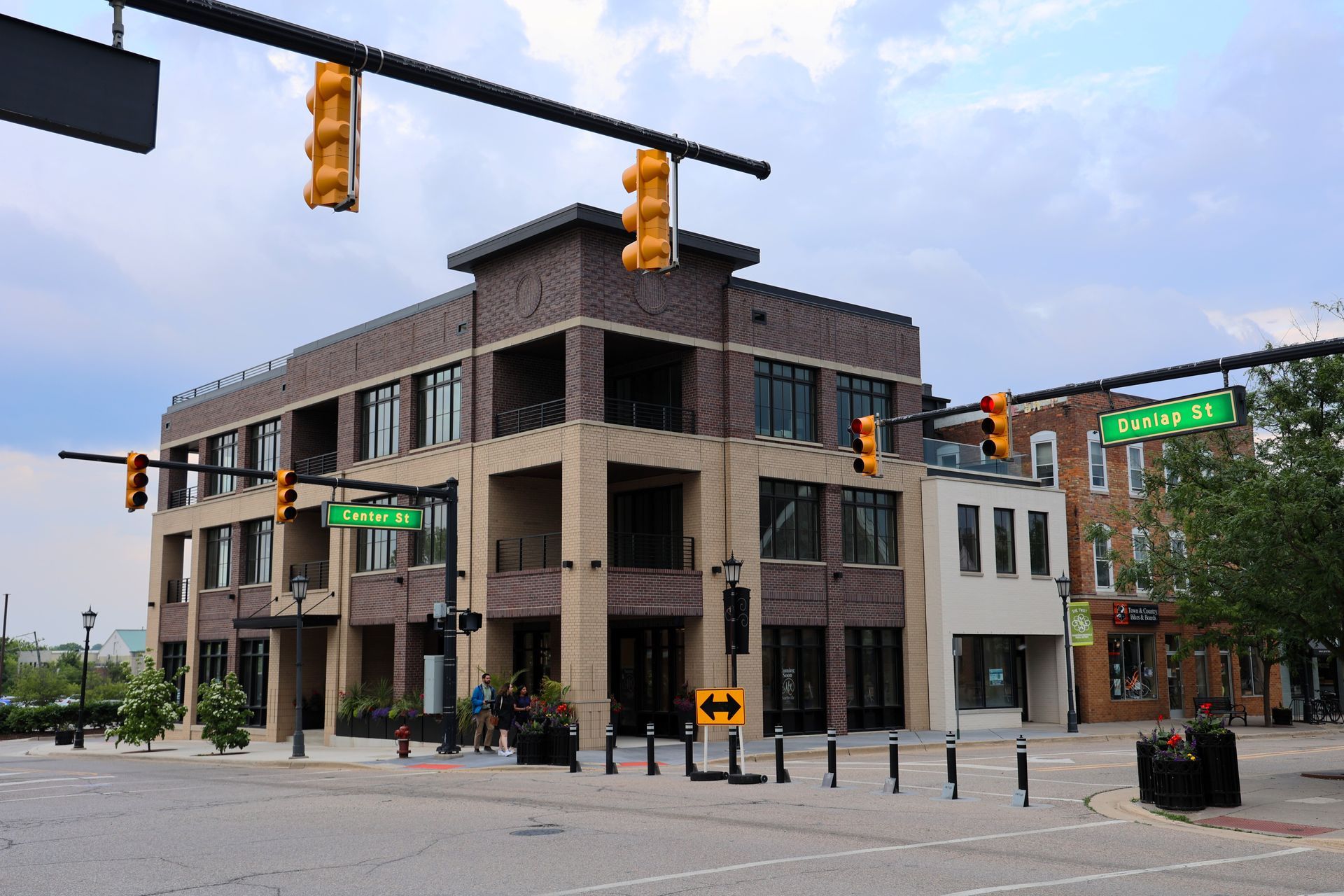 A multi-story brick building at a street corner with traffic lights, signs, and a clear sky.