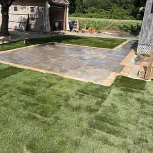 Newly installed patio with surrounding green lawn and a shed in the background.