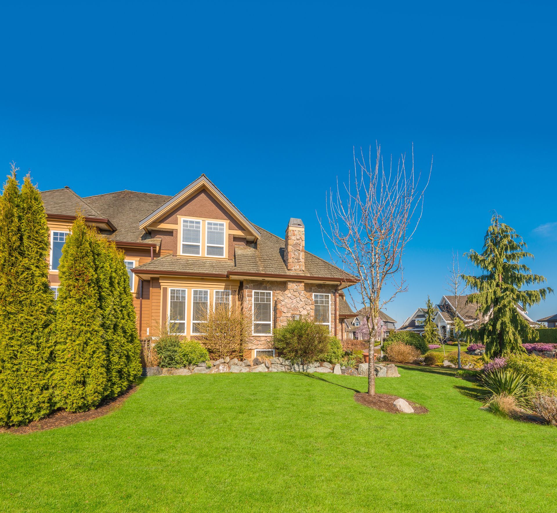Brick house with manicured green lawn, trees, and clear blue sky