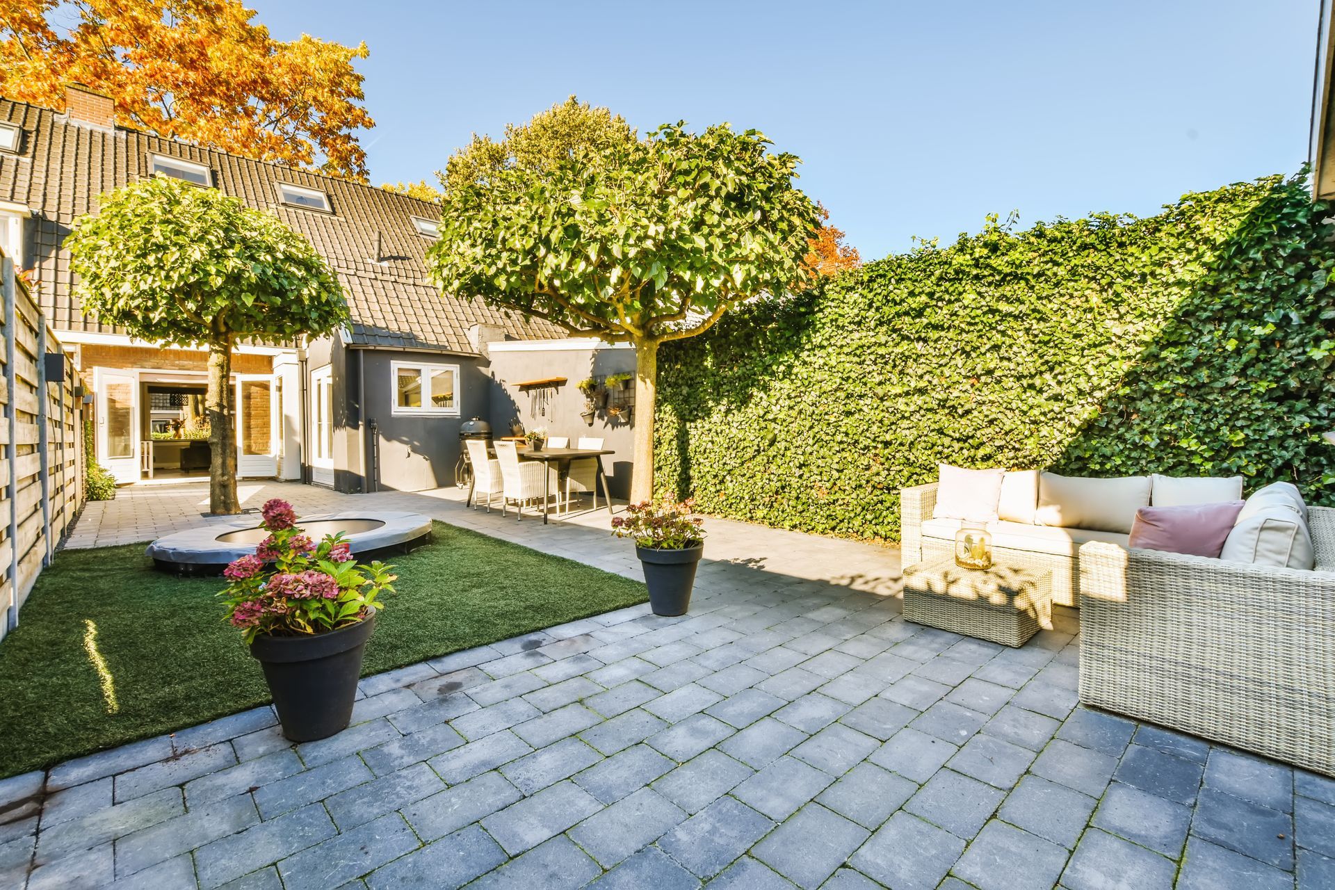 Sunny patio with stone pavers, potted flowers, outdoor seating, and ivy-covered walls