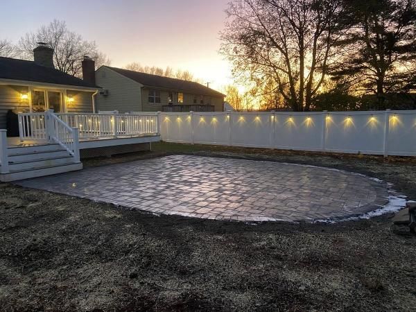 Backyard with a gravel base, white fence with lights, deck, and a sunset.