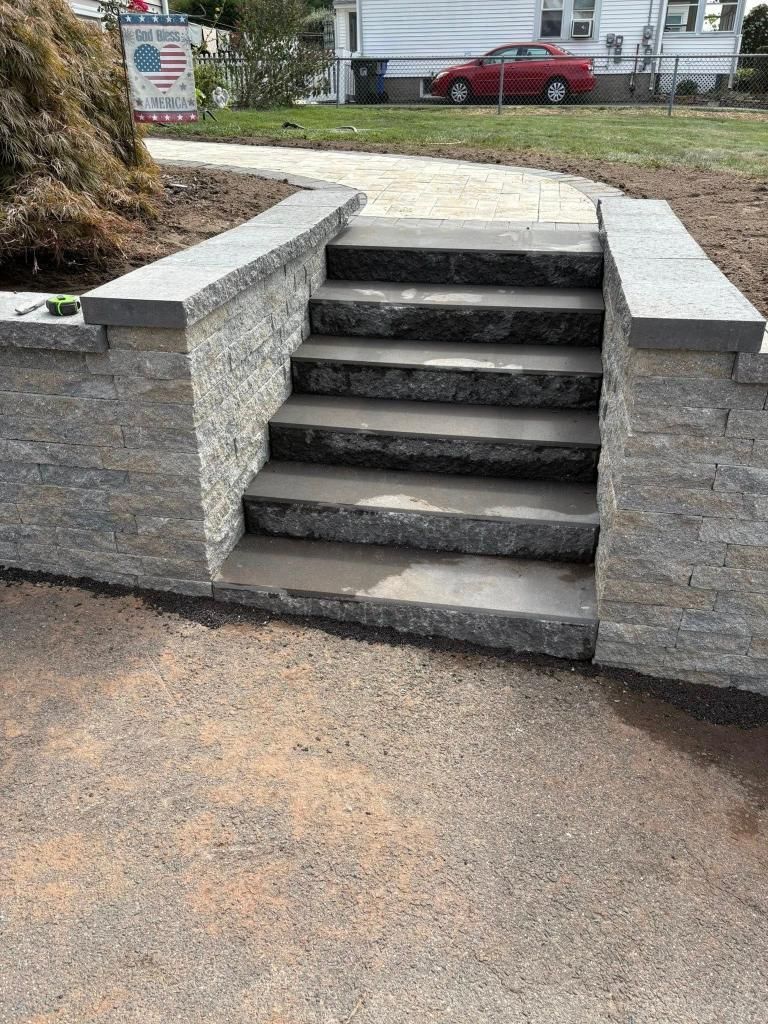 Stone steps leading up, framed by retaining walls. Gravel path in foreground; house in the background.