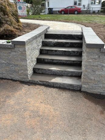 Stone steps leading up, framed by retaining walls. Gravel path in foreground; house in the background.