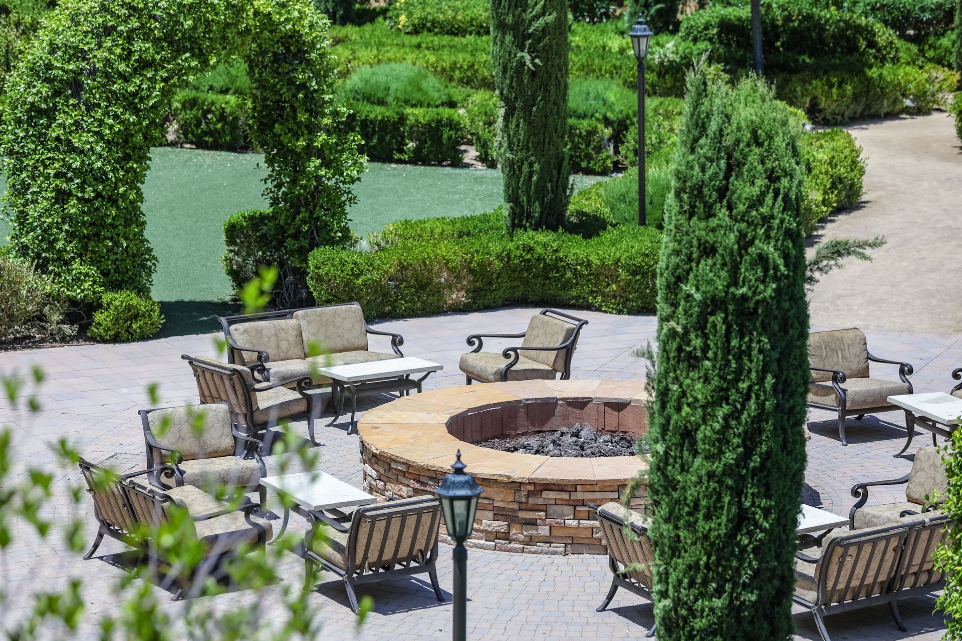 Outdoor patio with fire pit, seating, green hedges, and trees.