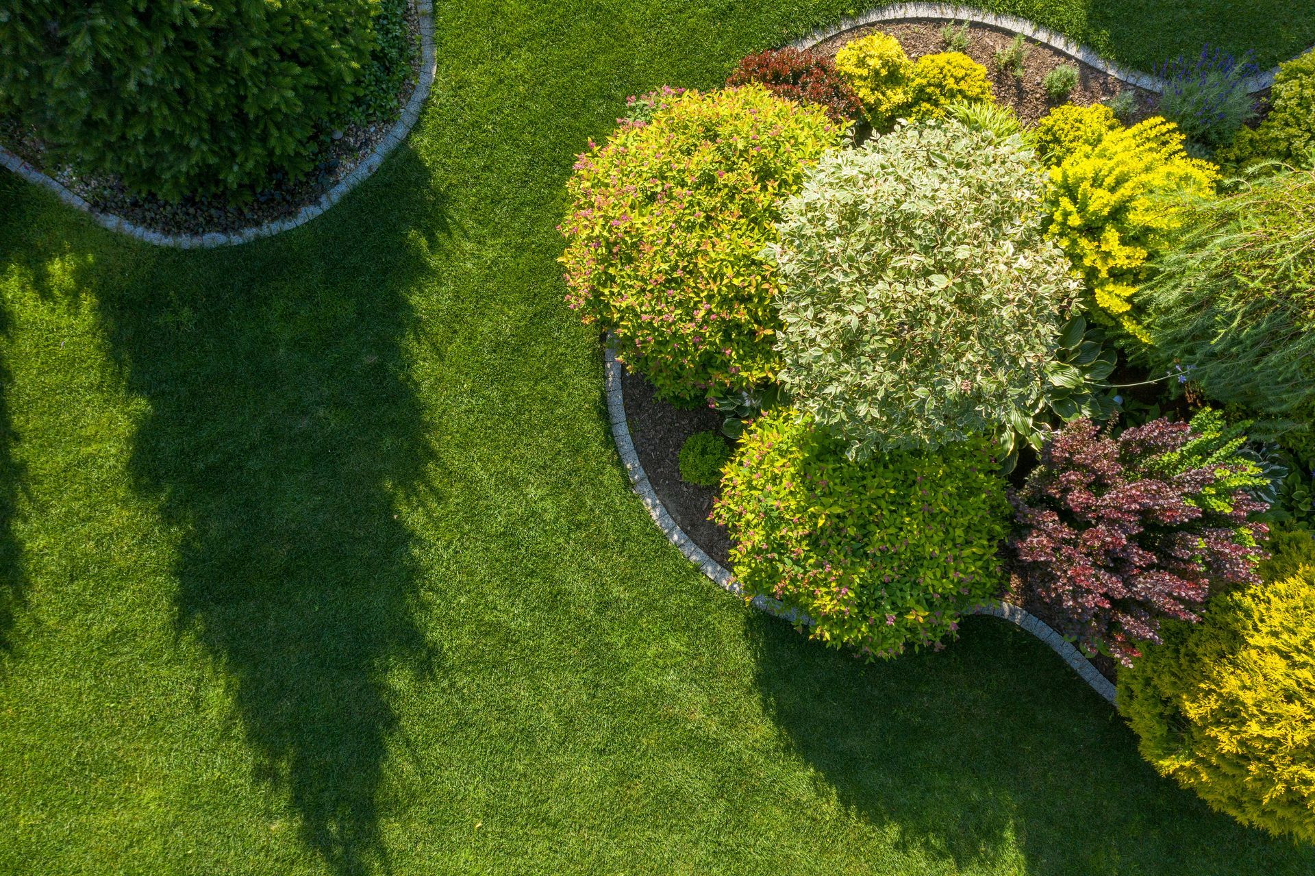 Overhead view of a manicured lawn with colorful shrubs and dark shadows.