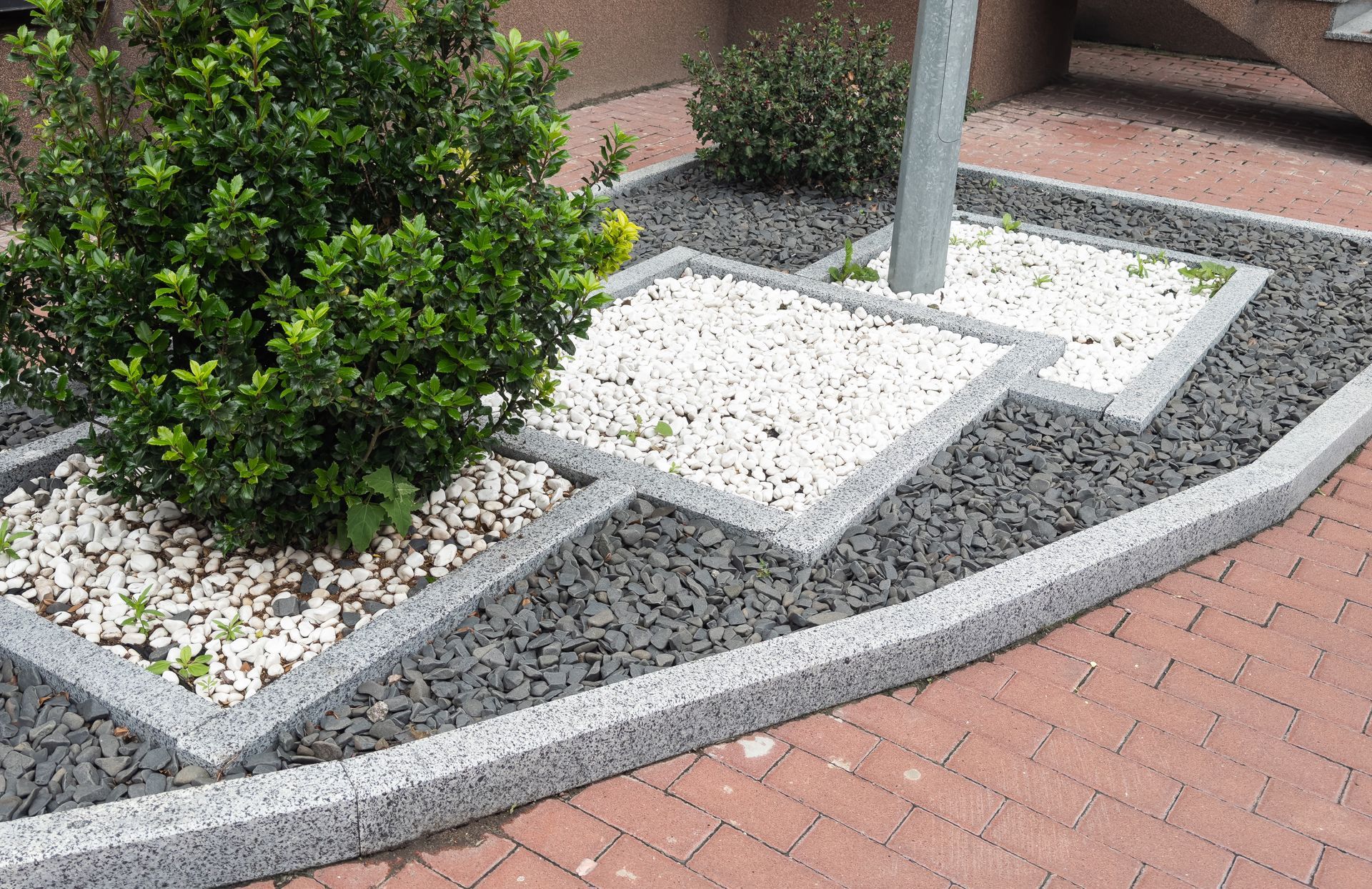 Curved concrete and brick landscaping around a small tree and pole, bordered by white gravel and stepping stones