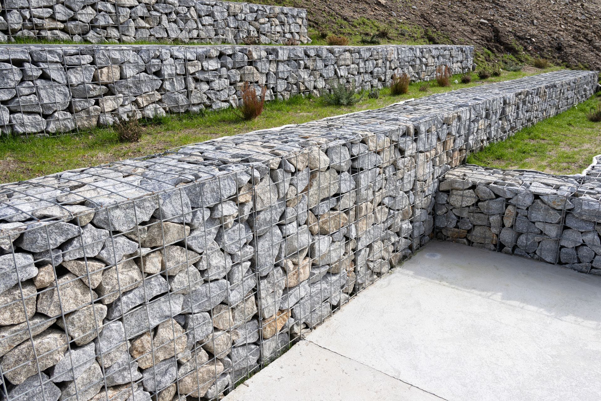 Stone terraced retaining walls made of gray rocks beside a concrete walkway outdoors