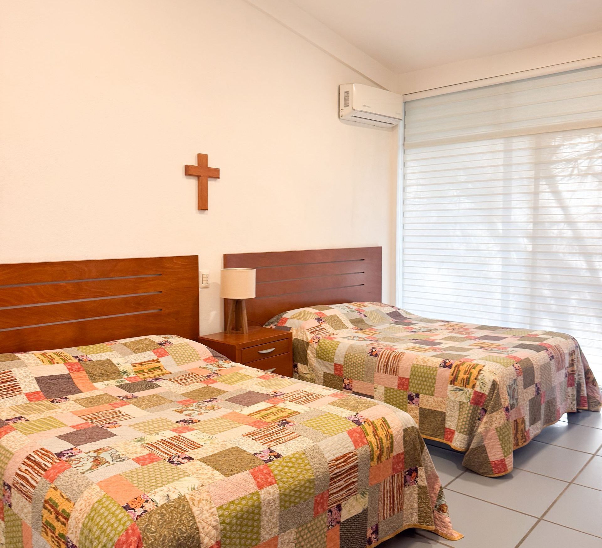 Un dormitorio con dos camas y una cruz en la pared.