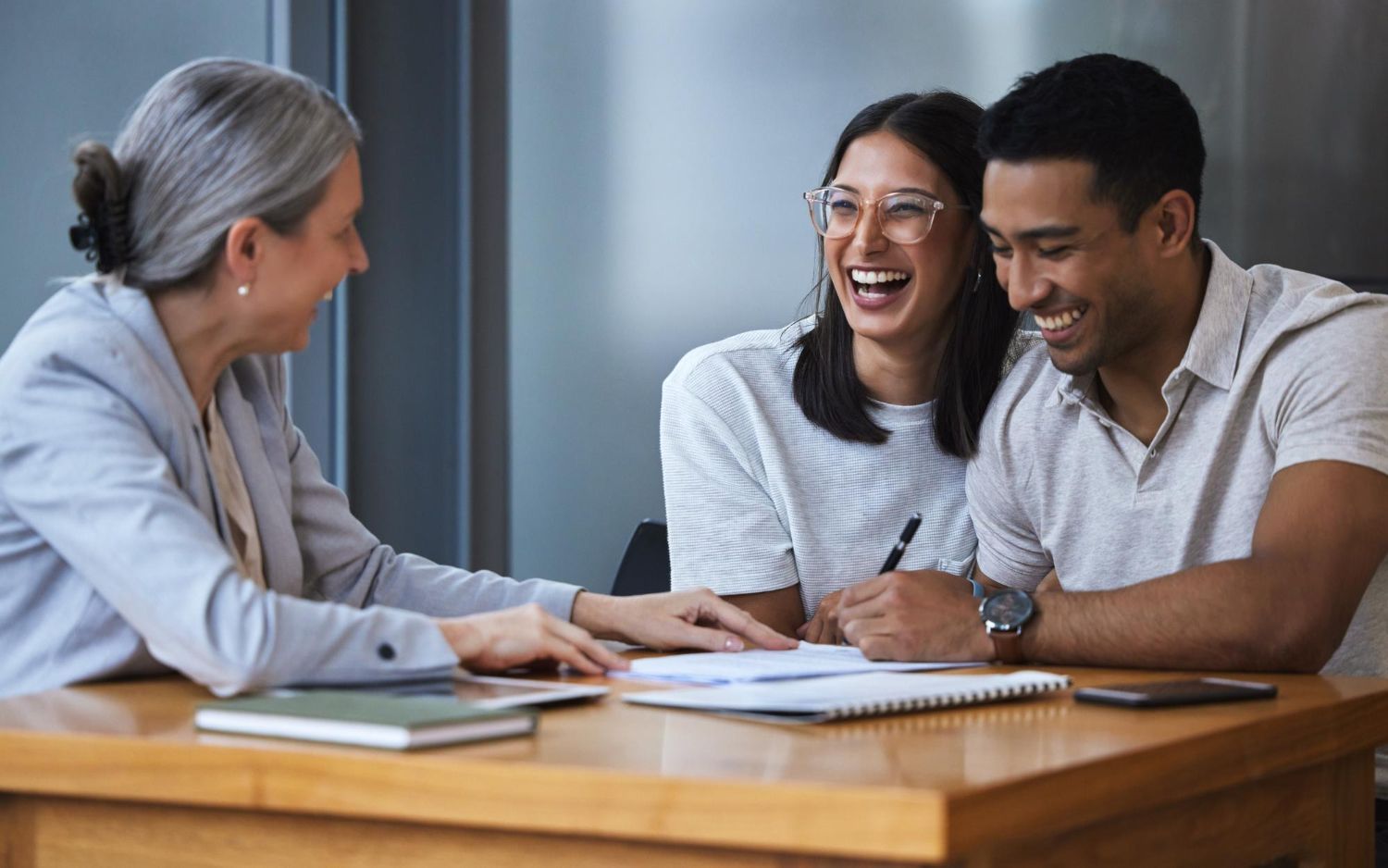 A couple laughs while reviewing paperwork with a professional in a modern office setting.