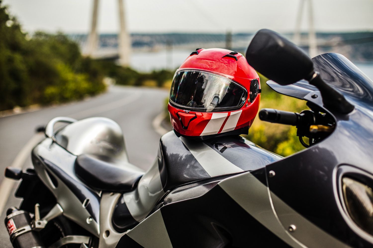 Red motorcycle helmet on a parked black and silver motorcycle, coastal road background.