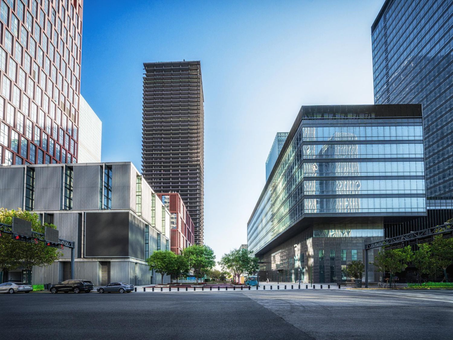 Modern cityscape with tall buildings, glass facades, and a street with parked cars under a blue sky.