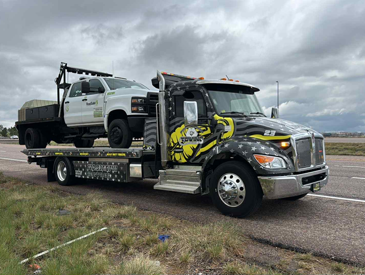 Tow truck hauling a white pickup truck on a highway under cloudy skies.