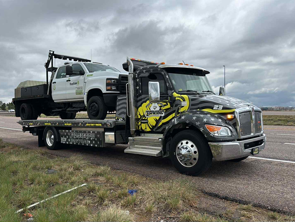 Tow truck hauling a white pickup truck on a highway under cloudy skies.