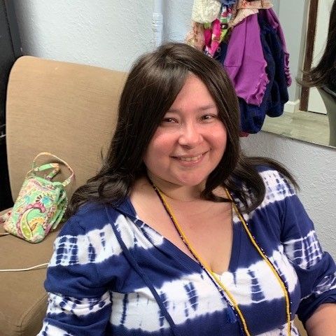 A woman in a yellow sweater is holding a wig and a brush.